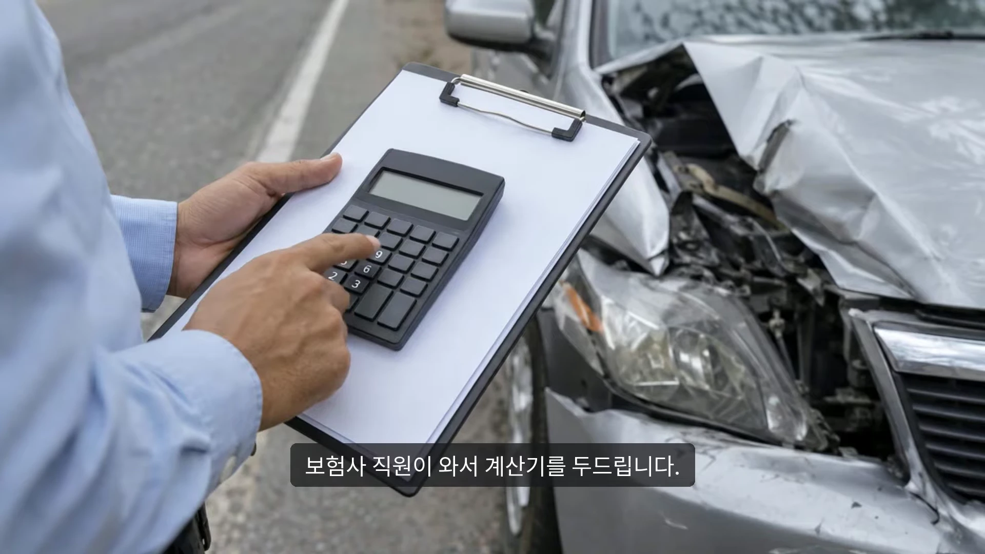 앞부분이 크게 파손된 은색 승용차 옆에서 하늘색 셔츠를 입은 보험사 직원이 클립보드를 들고 계산기를 두드리는 모습.