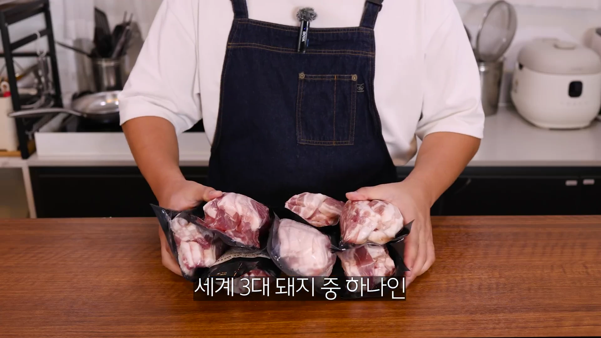 앞치마를 두른 사람이 500g씩 진공 포장된 삼겹살 팩들을 양손으로 모아 들고 있는 모습.