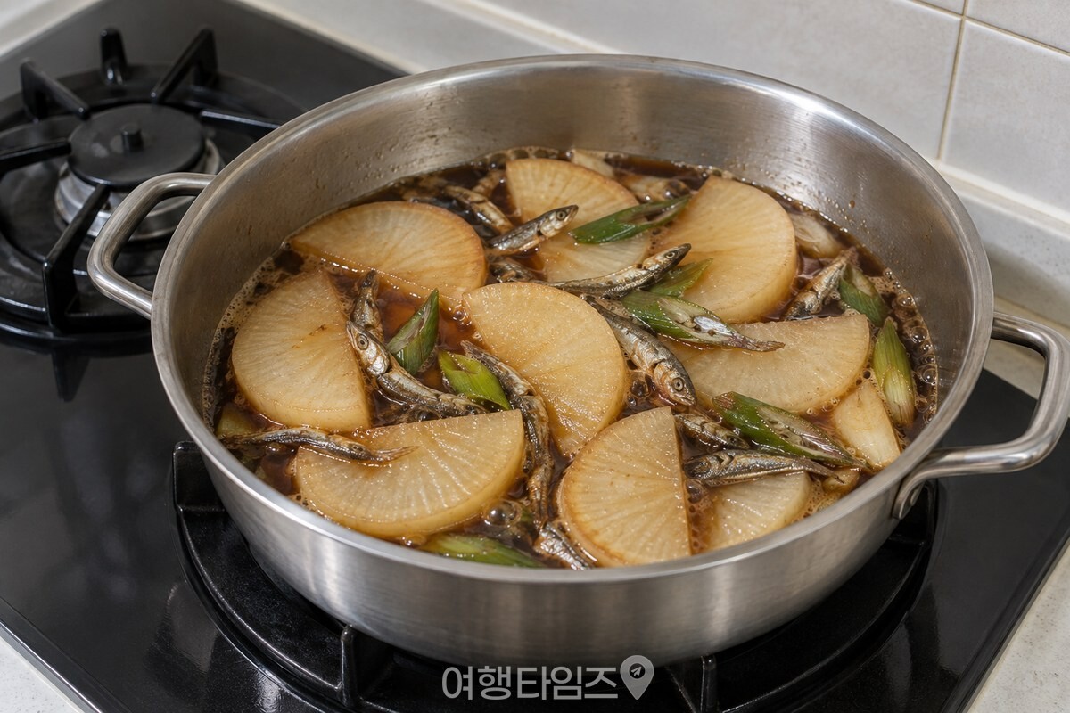 넓은 냄비에 반달 모양 무와 마른 멸치를 넣고 간장 양념에 졸인 모습. / 기사 이해를 돕기 위한 생성형 이미지