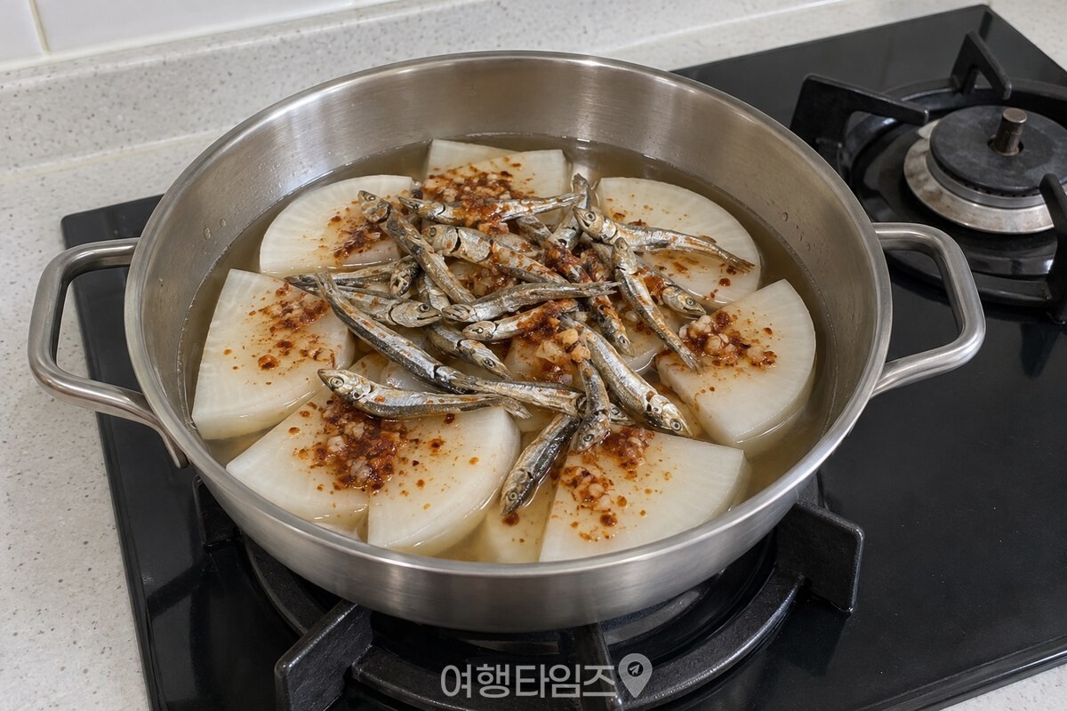 넓적한 냄비에 무를 한 겹으로 깔고 양념과 멸치를 올린 조리 전 상태. / 기사 이해를 돕기 위한 생성형 이미지