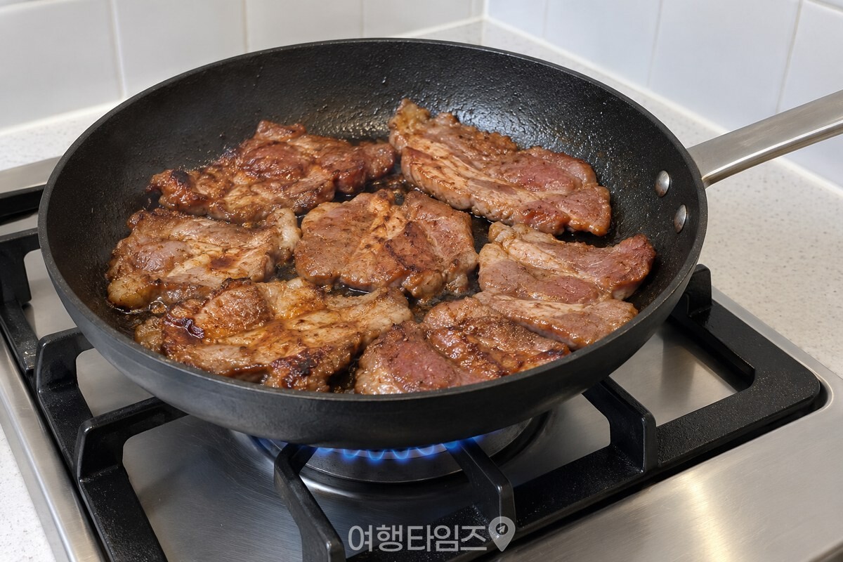 센 불의 팬에 양념한 돼지고기를 넓게 펴고 한쪽 면을 익히는 모습 / 기사 이해를 돕기 위한 생성형 이미지