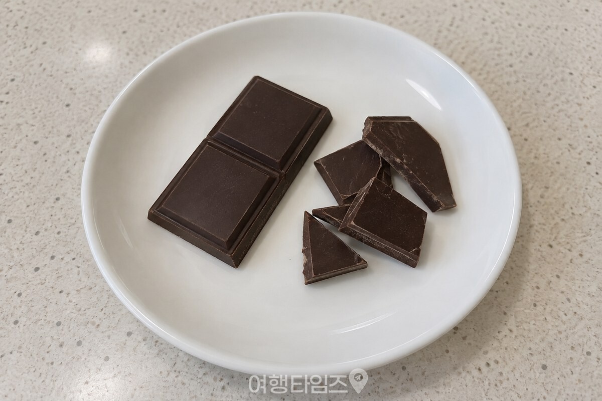 70% 이상 다크 초콜릿 한 조각과 잘게 쪼갠 조각을 작은 흰 접시에 담은 모습. / 기사 이해를 돕기 위한 생성형 이미지