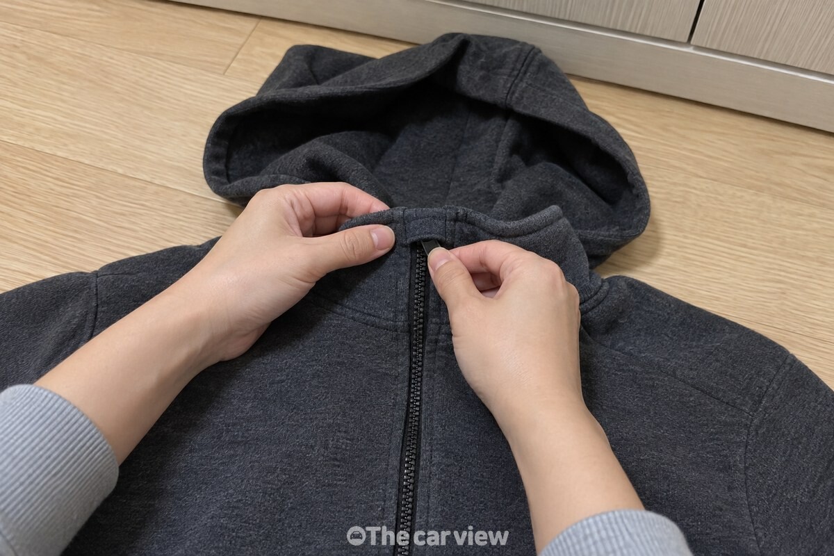 손이 후드집업 지퍼를 턱 밑까지 끝까지 올리고 손잡이를 깃 안쪽으로 접어 넣고 있다. / 기사 이해를 돕기 위한 생성형 이미지