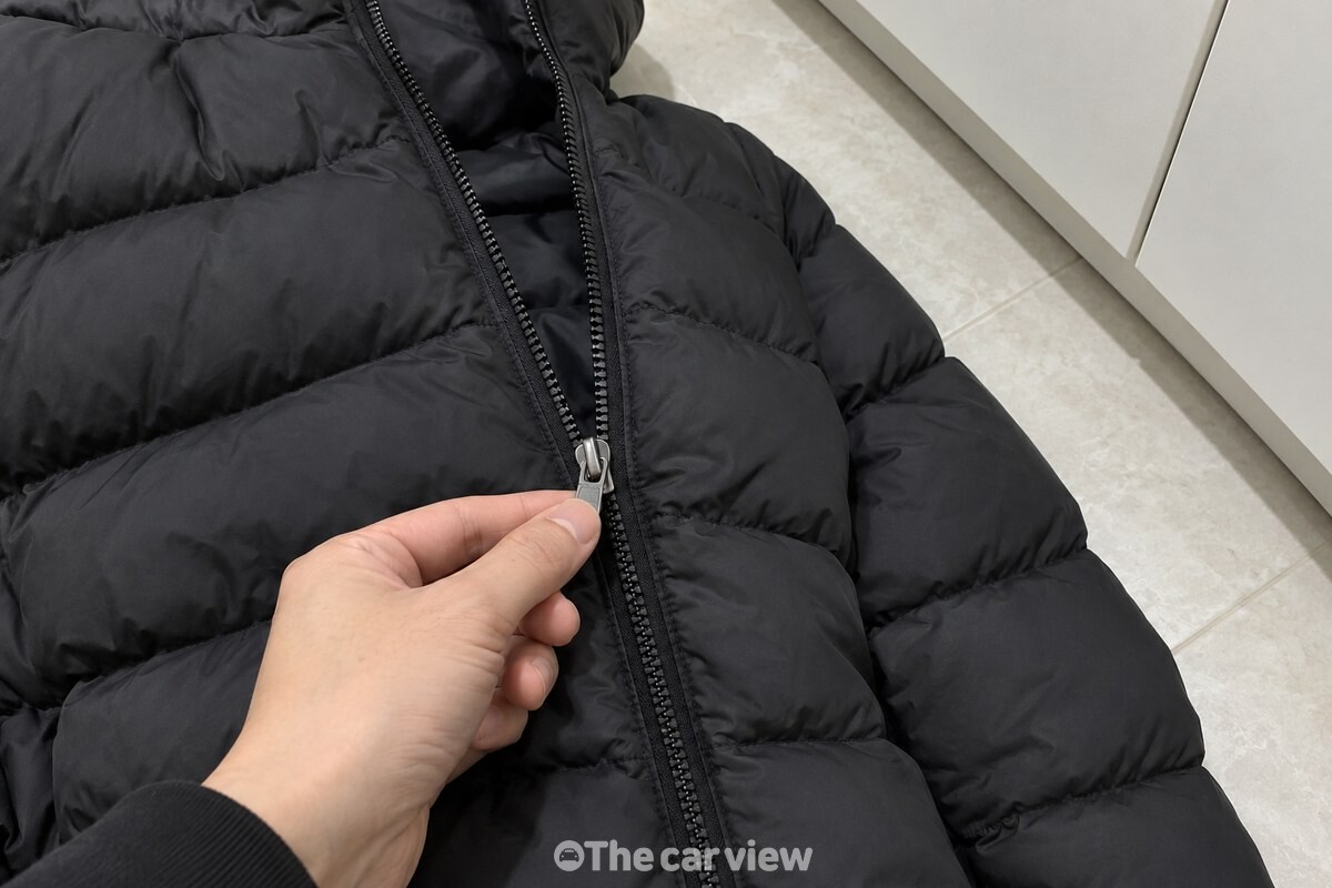 깨끗한 현관 앞에서 검은 패딩의 앞지퍼 이빨과 손잡이를 가까이 보여 주는 모습 / 기사 이해를 돕기 위한 생성형 이미지