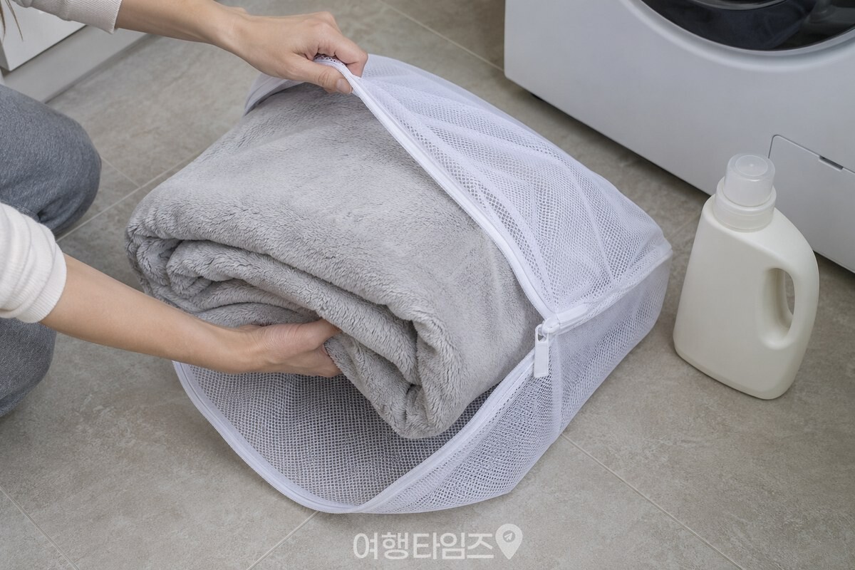 반으로 접은 극세사 이불을 큰 세탁망에 넣는 손과 액체 중성세제가 보인다. / 기사 이해를 돕기 위한 생성형 이미지