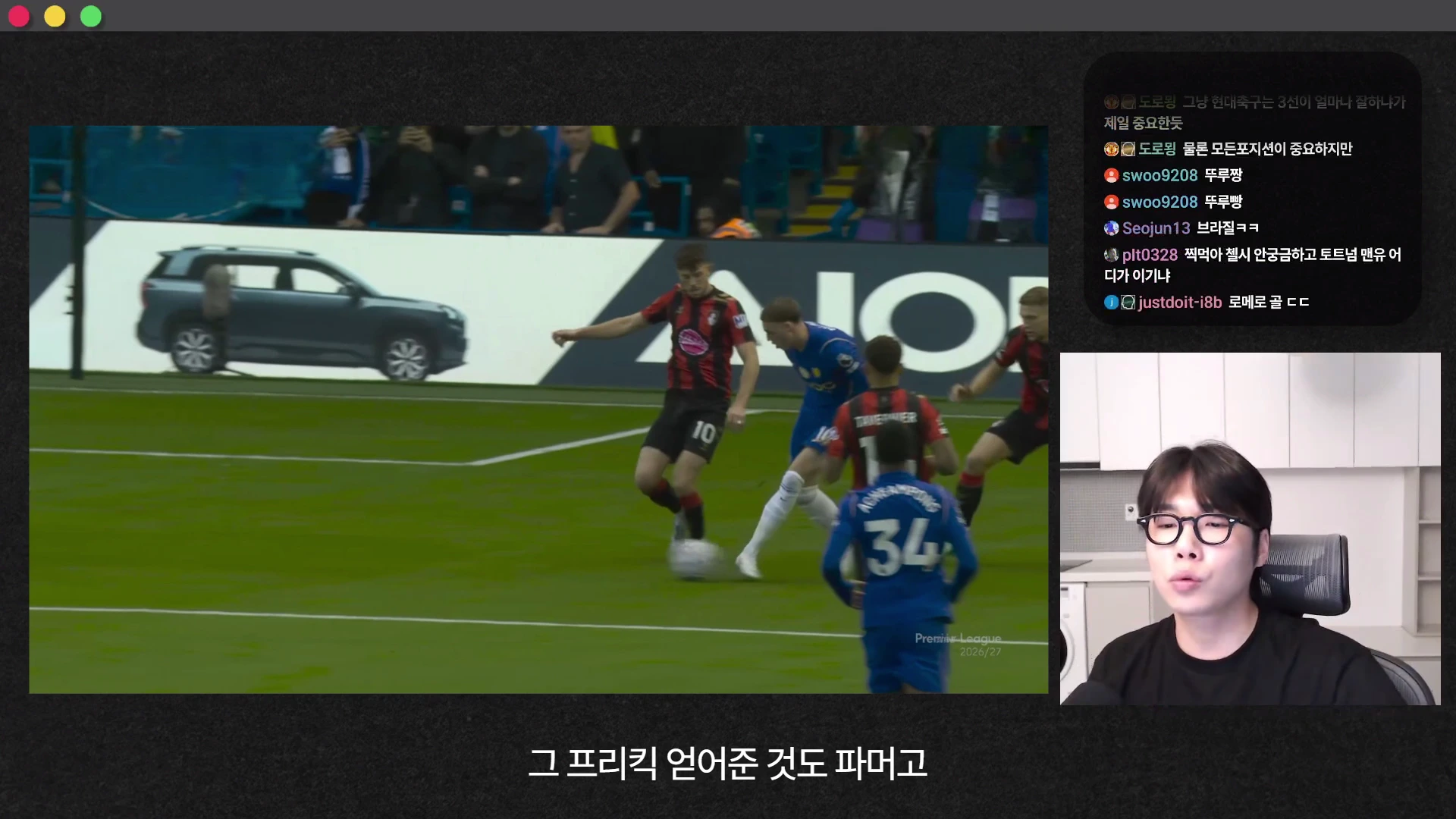 축구 경기 중 파란색 유니폼을 입은 선수가 상대 수비진 사이에서 공을 몰고 나가는 장면이 왼쪽에 나타나고, 오른쪽에는 안경을 쓴 남성이 방송을 진행하는 모습이 보입니다.