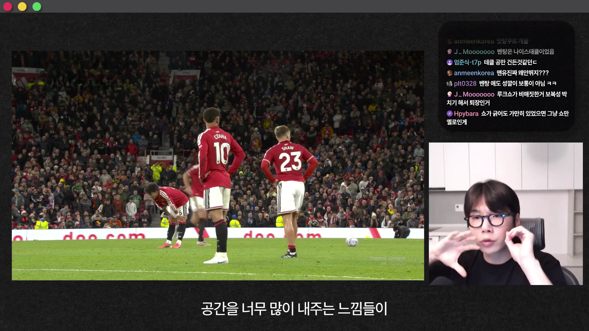 축구 경기 중 맨체스터 유나이티드 선수들이 그라운드에 서 있는 모습이 담긴 화면과 우측 하단에는 안경을 쓴 남성이 방송을 진행하는 모습이 보이며 상단에는 실시간 채팅창이 떠 있습니다.