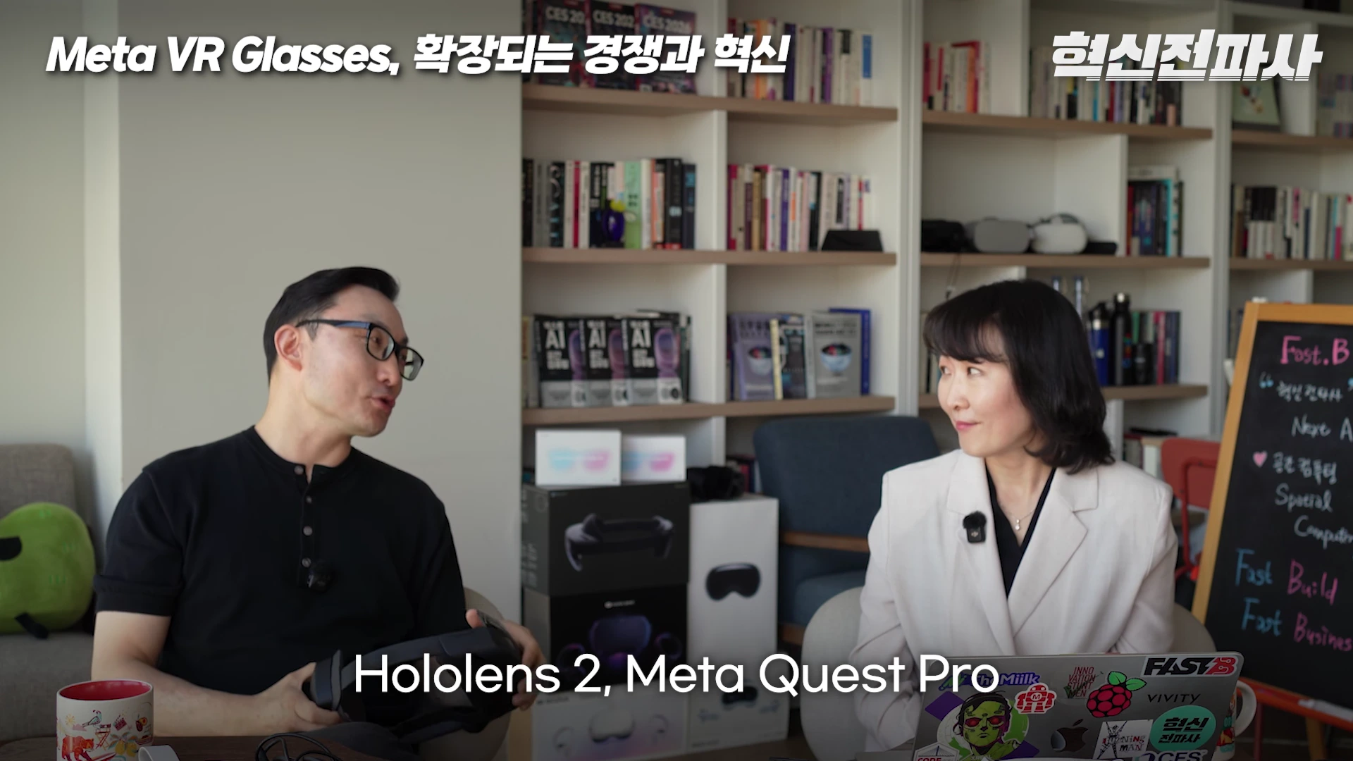 두 사람이 책장이 있는 서재 같은 공간에서 의자에 앉아 대화를 나누고 있으며, 왼쪽 남성은 손에 VR 기기를 들고 있고 오른쪽 여성은 노트북을 앞에 두고 이야기를 듣고 있다.