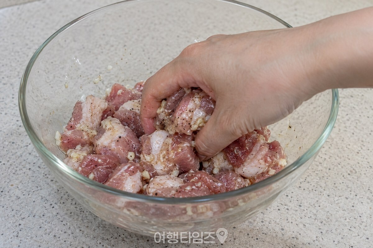 한 손이 매실액과 마늘로 밑간한 돼지고기를 유리 볼에서 고루 버무리고 있다. / 기사 이해를 돕기 위한 생성형 이미지