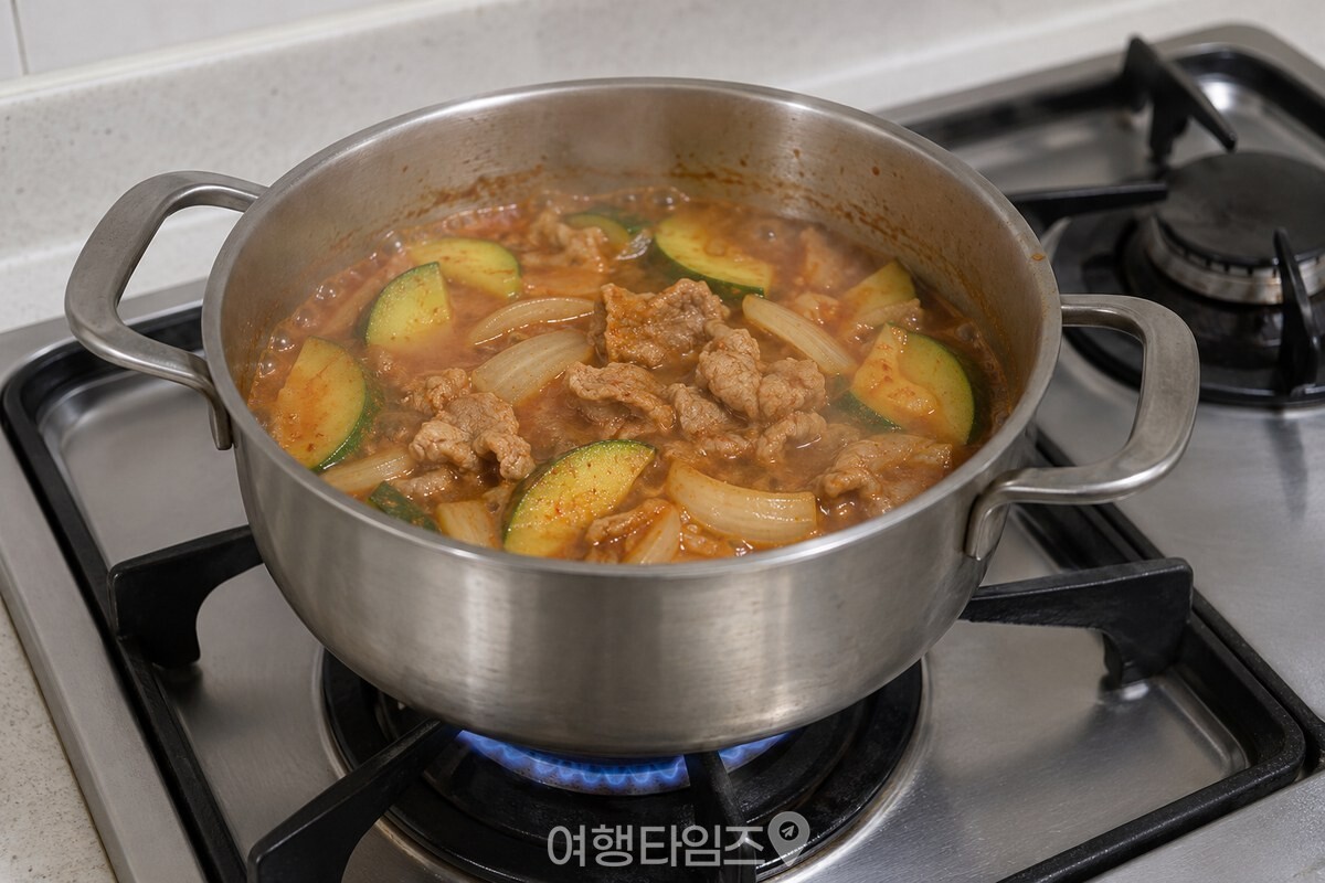 끓는 붉은 국물 속에 반달 애호박과 양파, 돼지고기가 고르게 익고 있다. / 기사 이해를 돕기 위한 생성형 이미지