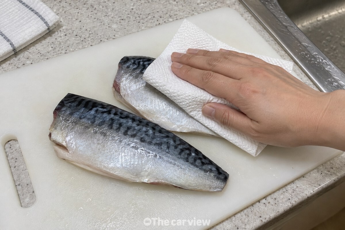 키친타월로 고등어 토막의 껍질과 살 표면 물기를 누르고 있다. / 기사 이해를 돕기 위한 생성형 이미지