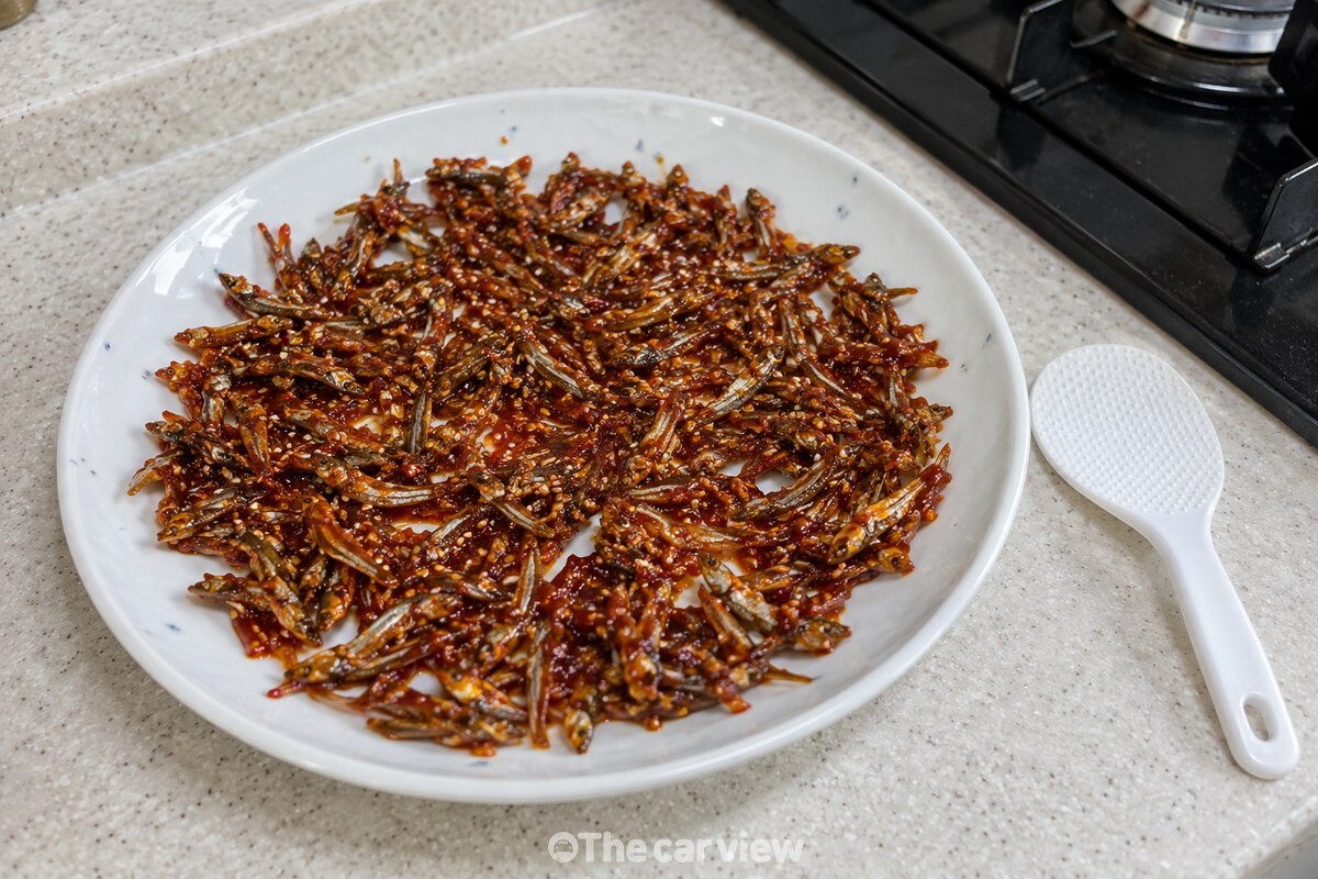 흰 반찬 접시에 넓게 펼쳐 식히는 고추장 멸치볶음과 옆에 놓인 작은 흰 주걱. / 기사 이해를 돕기 위한 생성형 이미지