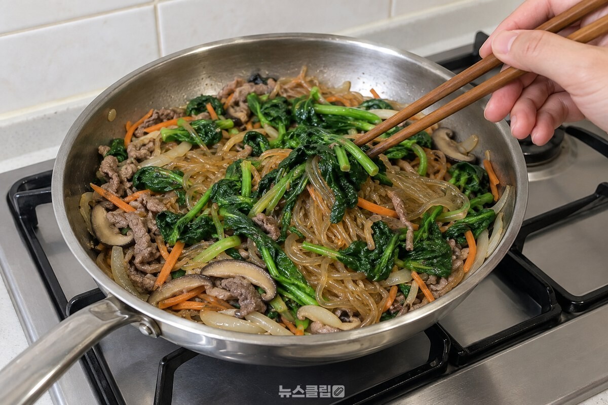 불을 끈 팬 안의 잡채 위에 밑간한 시금치를 올려 젓가락으로 섞는 모습. / 기사 이해를 돕기 위한 생성형 이미지