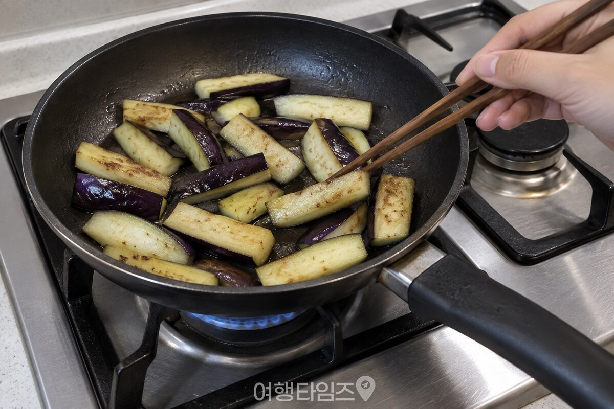 약불의 가스레인지 팬에서 젓가락으로 가지를 뒤적이는 모습 / 기사 이해를 돕기 위한 생성형 이미지