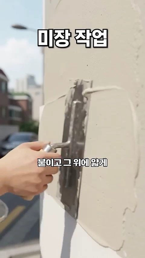 건물 외벽에 미장용 흙손을 사용하여 마감재를 얇게 펴 바르는 모습이 담긴 클로즈업 영상 화면