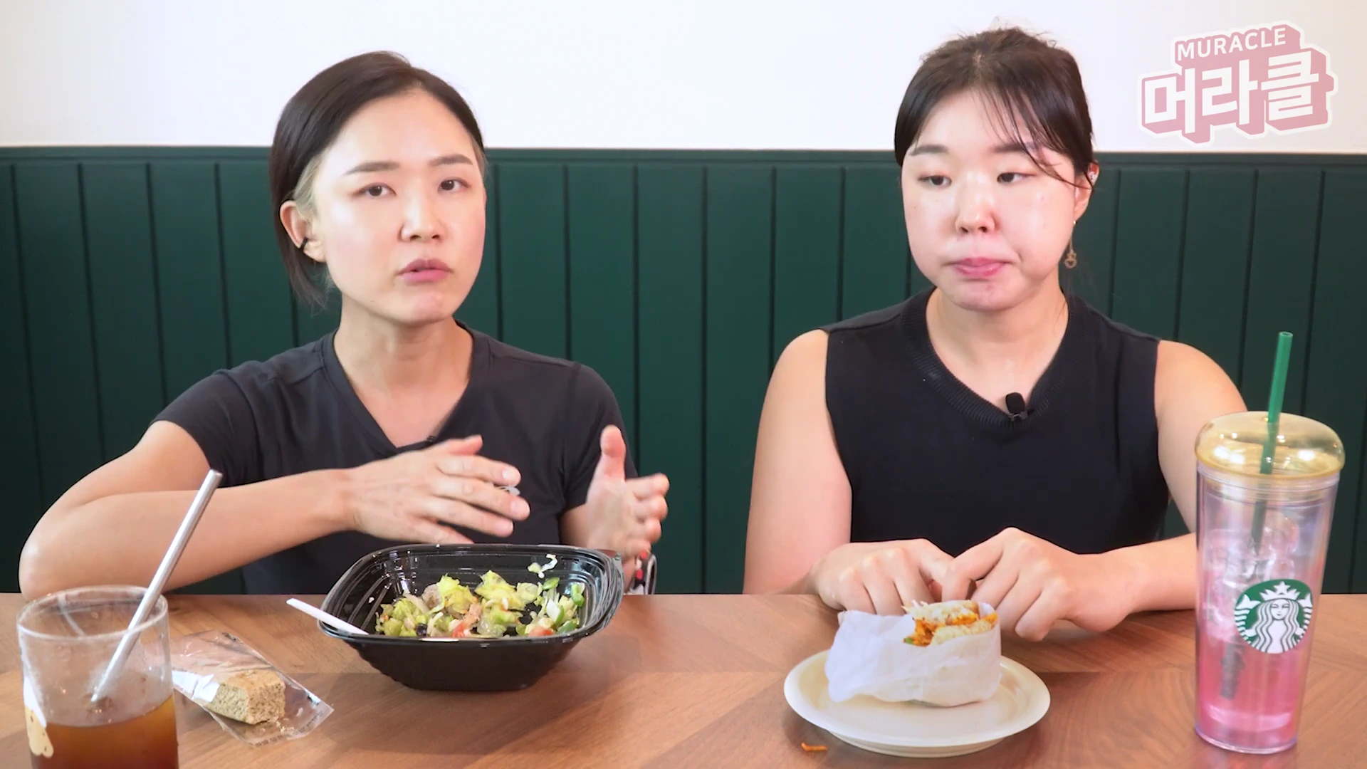 두 여성이 식탁에 앉아 샐러드와 샌드위치를 먹으며 대화를 나누고 있다.