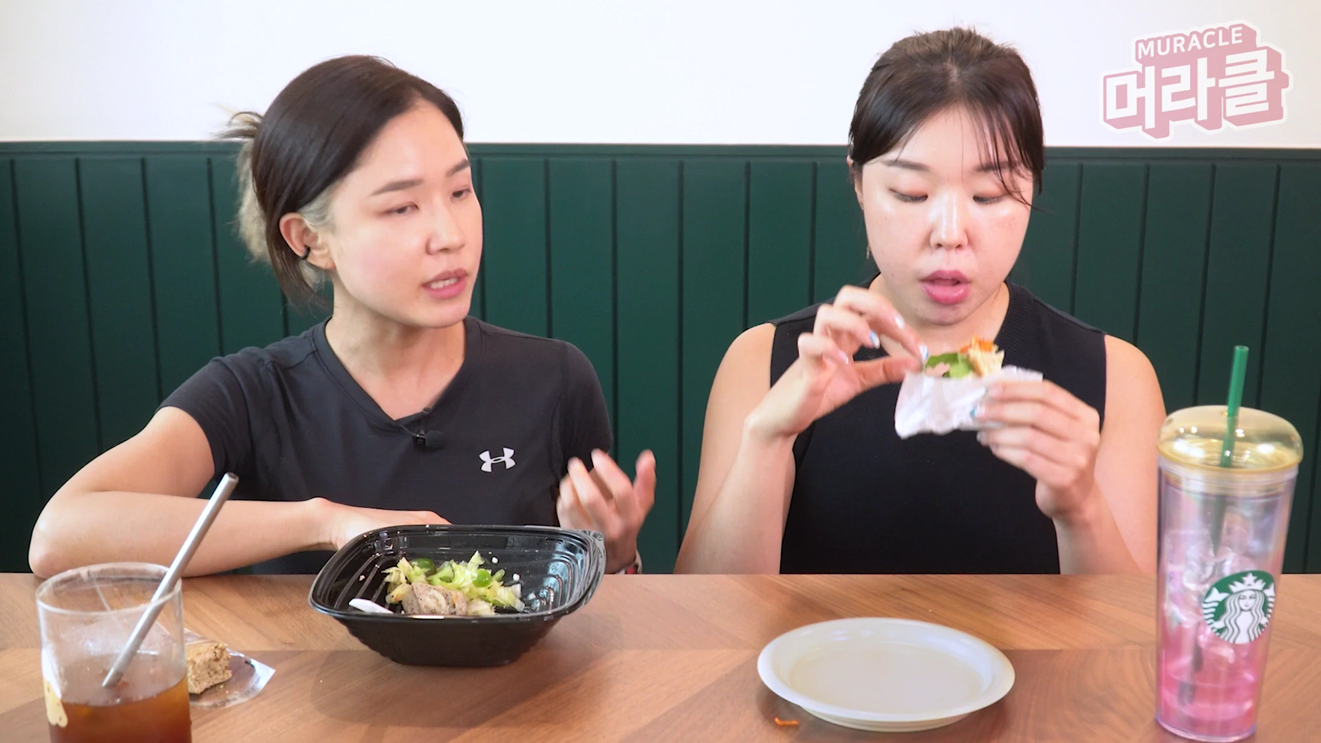 두 명의 여성이 테이블에 앉아 샐러드와 샌드위치를 먹으며 대화하고 있는 모습