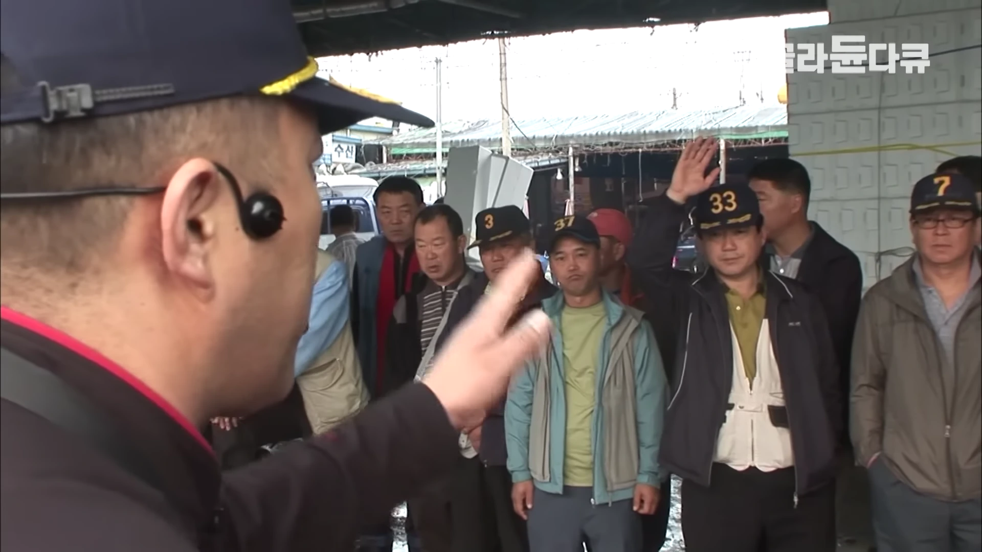 수산물 경매장에서 중도매인이 손을 들어 가격을 제시하자, 모자를 쓴 경매사가 이를 확인하며 경매를 진행하는 모습이다.