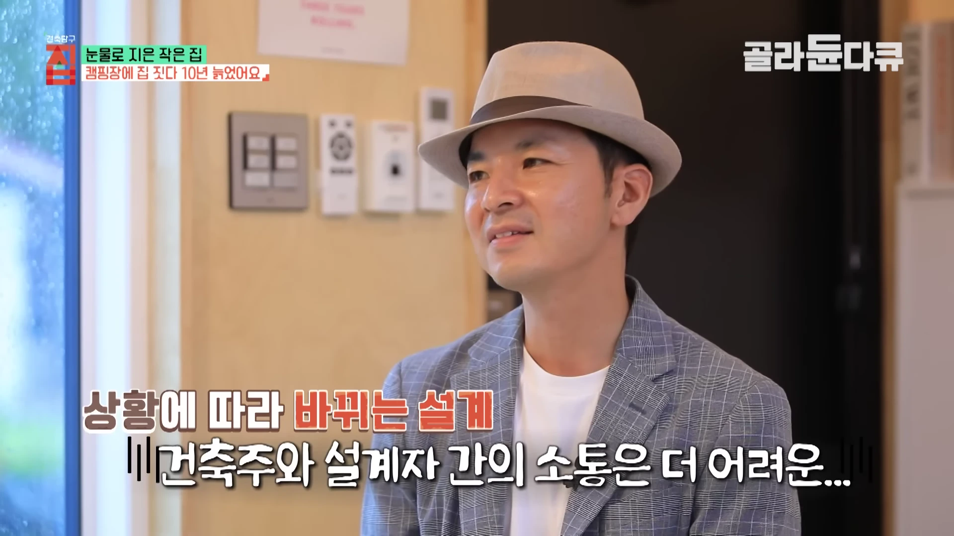 페도라를 쓰고 체크무늬 재킷을 입은 중년 남성이 실내에서 인터뷰하는 모습. 화면 하단에는 '상황에 따라 바뀌는 설계, 건축주와 설계자 간의 소통은 더 어려운...'이라는 자막이 적혀 있다.