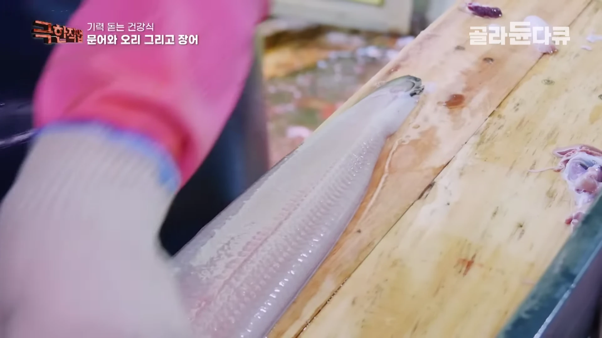 작업자가 나무 도마 위에서 장어를 손질하고 있는 모습을 근접 촬영한 영상 화면이다.
