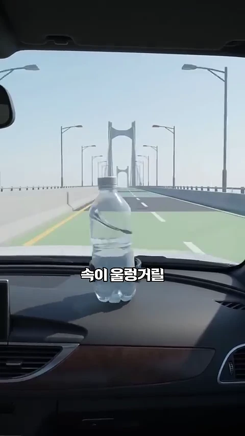 자동차 대시보드 위 컵홀더에 놓인 물병이 다리의 심한 흔들림으로 인해 크게 일렁이는 모습이 담긴 영상 캡처 화면입니다.