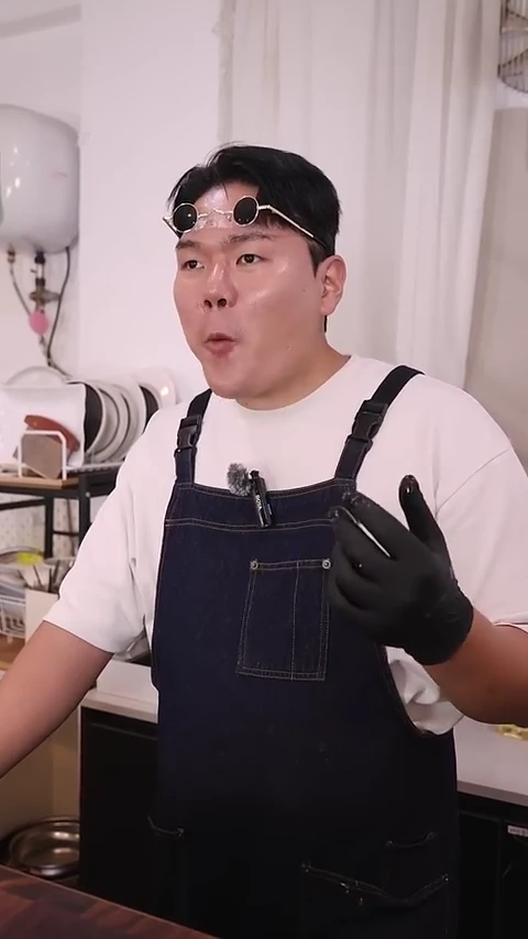 흰색 티셔츠와 앞치마를 입고 검은색 위생 장갑을 낀 남성이 머리 위로 선글라스를 올린 채 고기를 시식하고 있다.