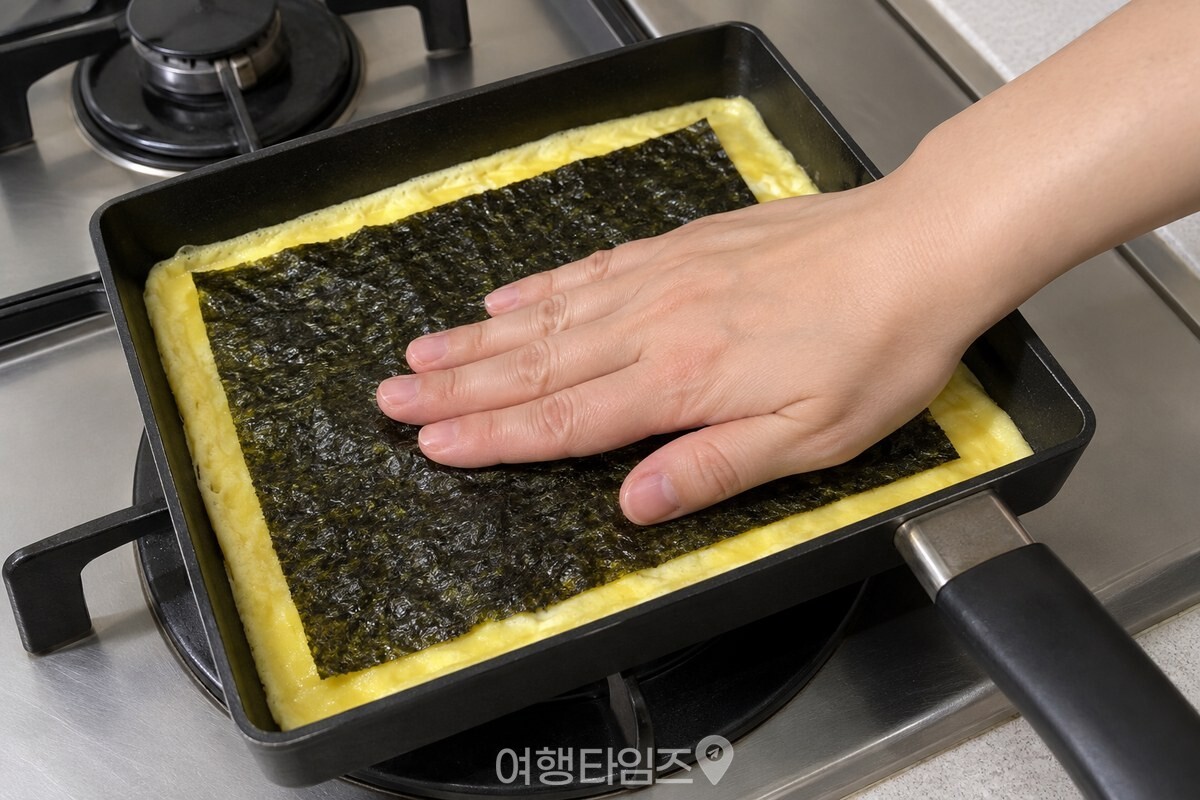 가장자리가 익은 얇은 계란 위에 김 한 장을 올려 손바닥으로 붙이는 모습 / 기사 이해를 돕기 위한 생성형 이미지