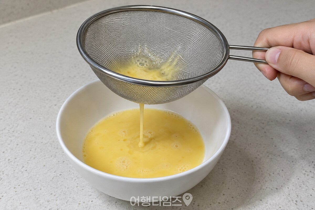 고운 스테인리스 체로 푼 계란물을 흰 그릇에 거르고 있다. / 기사 이해를 돕기 위한 생성형 이미지