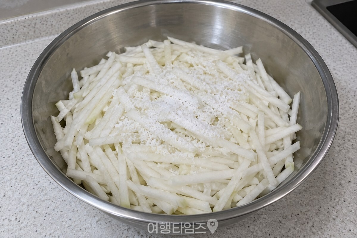 넓은 스테인리스 그릇의 무채 위에 소금이 고르게 뿌려진 절임 단계다. / 기사 이해를 돕기 위한 생성형 이미지