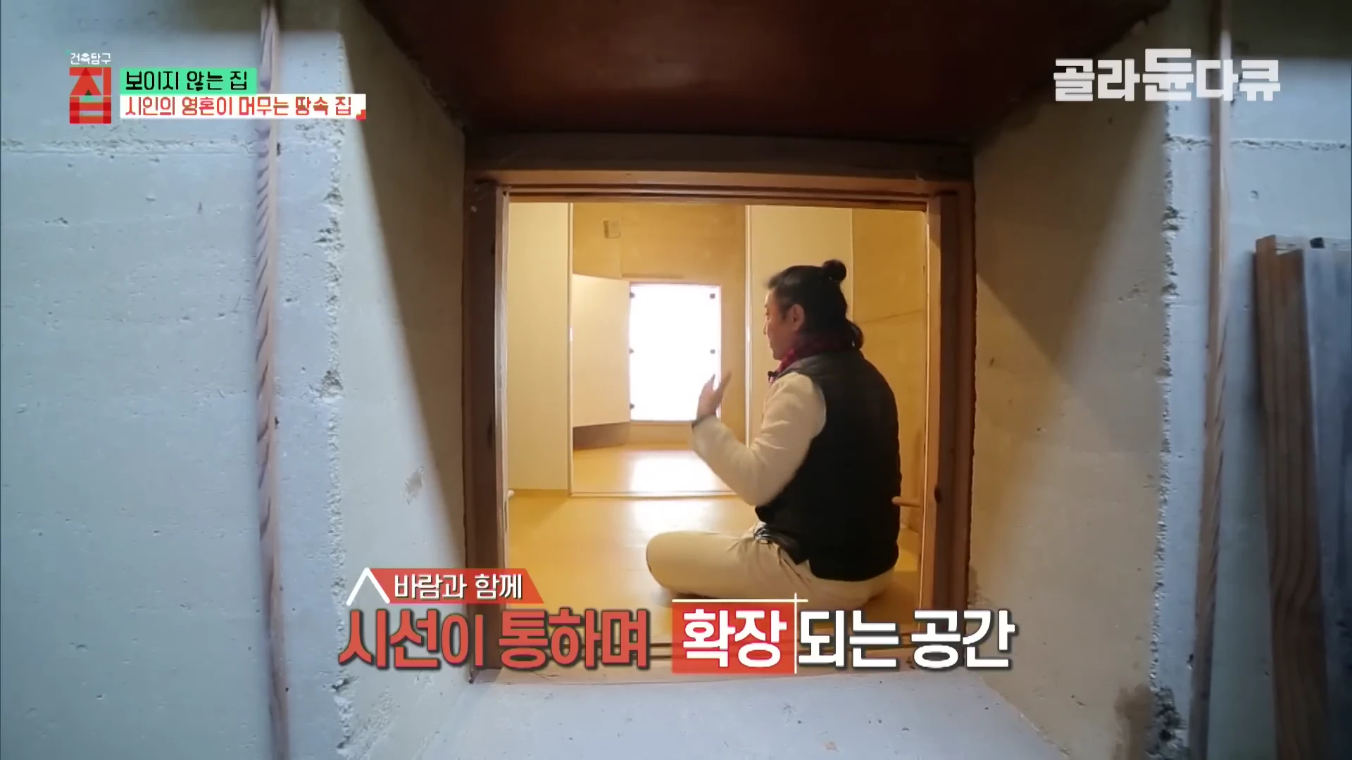 실내에서 한 남성이 좁은 문을 통해 다른 방을 가리키며 설명하는 모습이 담긴 방송 화면이며, 벽면에는 '바람과 함께 시선이 통하며 확장되는 공간'이라는 자막이 적혀 있다.
