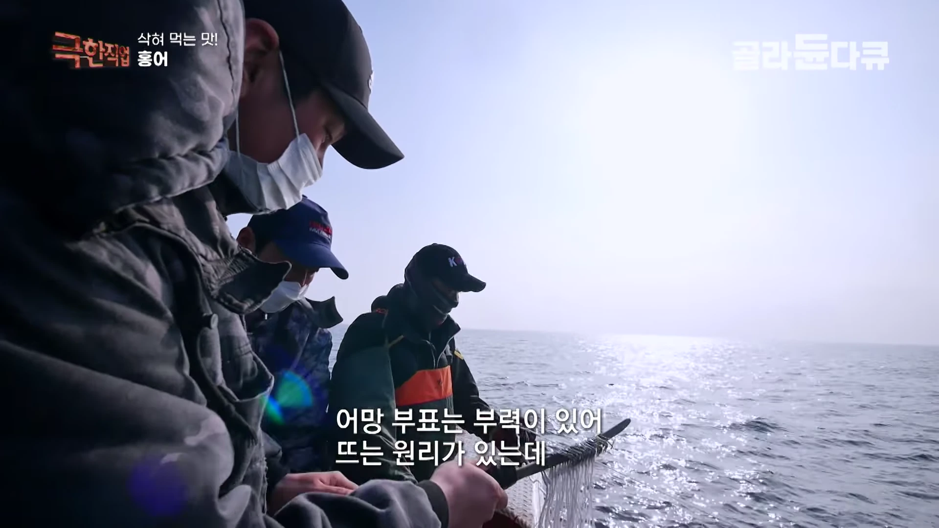 배 위에서 작업복과 마스크를 착용한 사람들이 어망을 바다로 흘려보내고 있는 모습