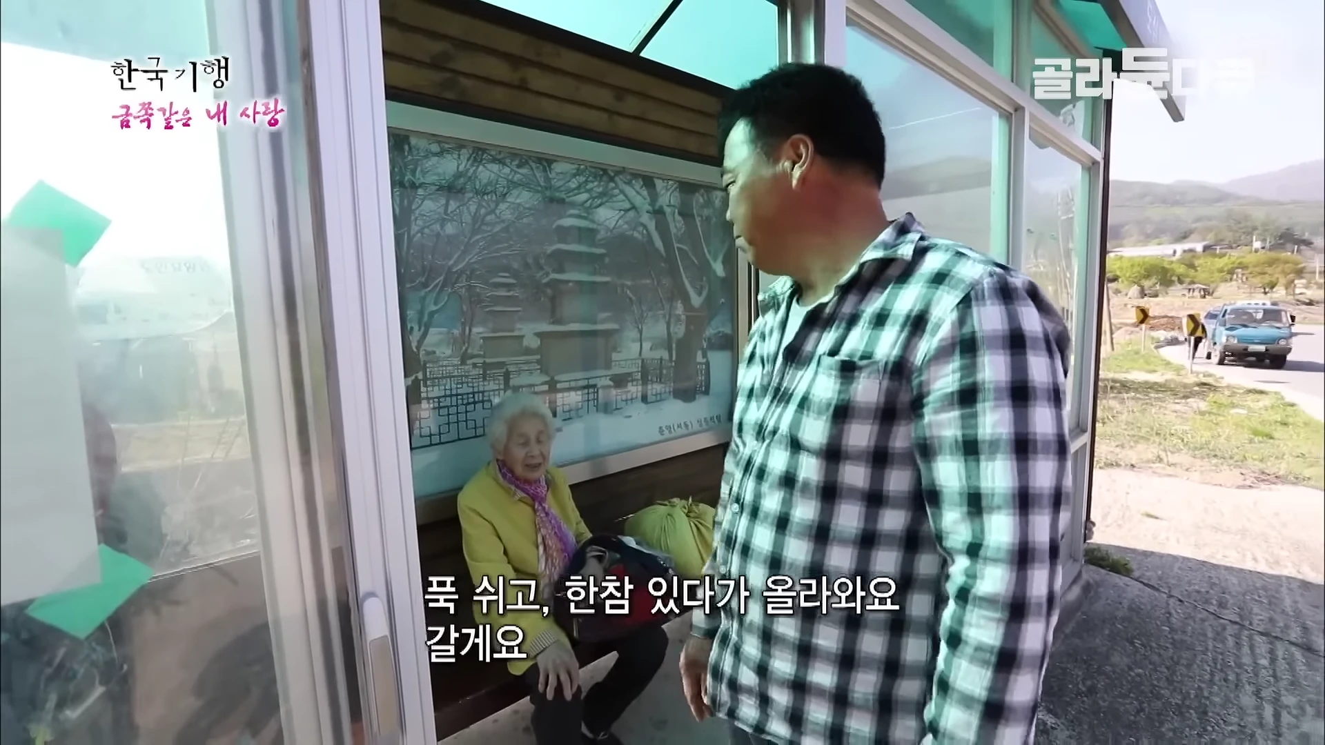 정류장 의자에 앉아 있는 노란색 옷을 입은 할머니와 옆에 서 있는 체크무늬 셔츠를 입은 중년 남성