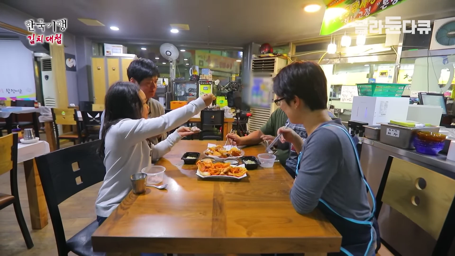 실내 식당 테이블에 네 명의 사람들이 둘러앉아 문어 김치를 함께 나누어 먹고 있는 모습입니다.