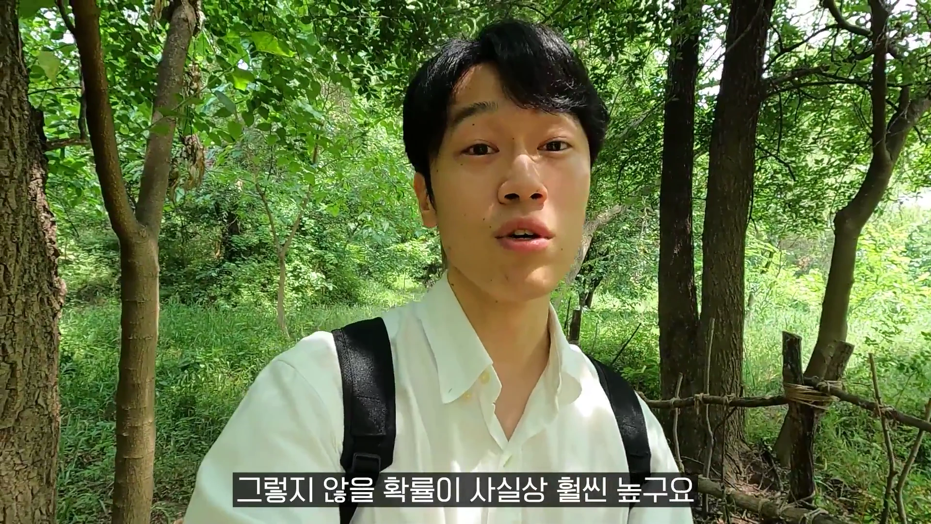 푸른 숲길을 배경으로 흰 셔츠를 입은 젊은 남성이 카메라를 보며 이야기를 나누고 있는 모습이 담긴 영상 캡처 화면입니다.