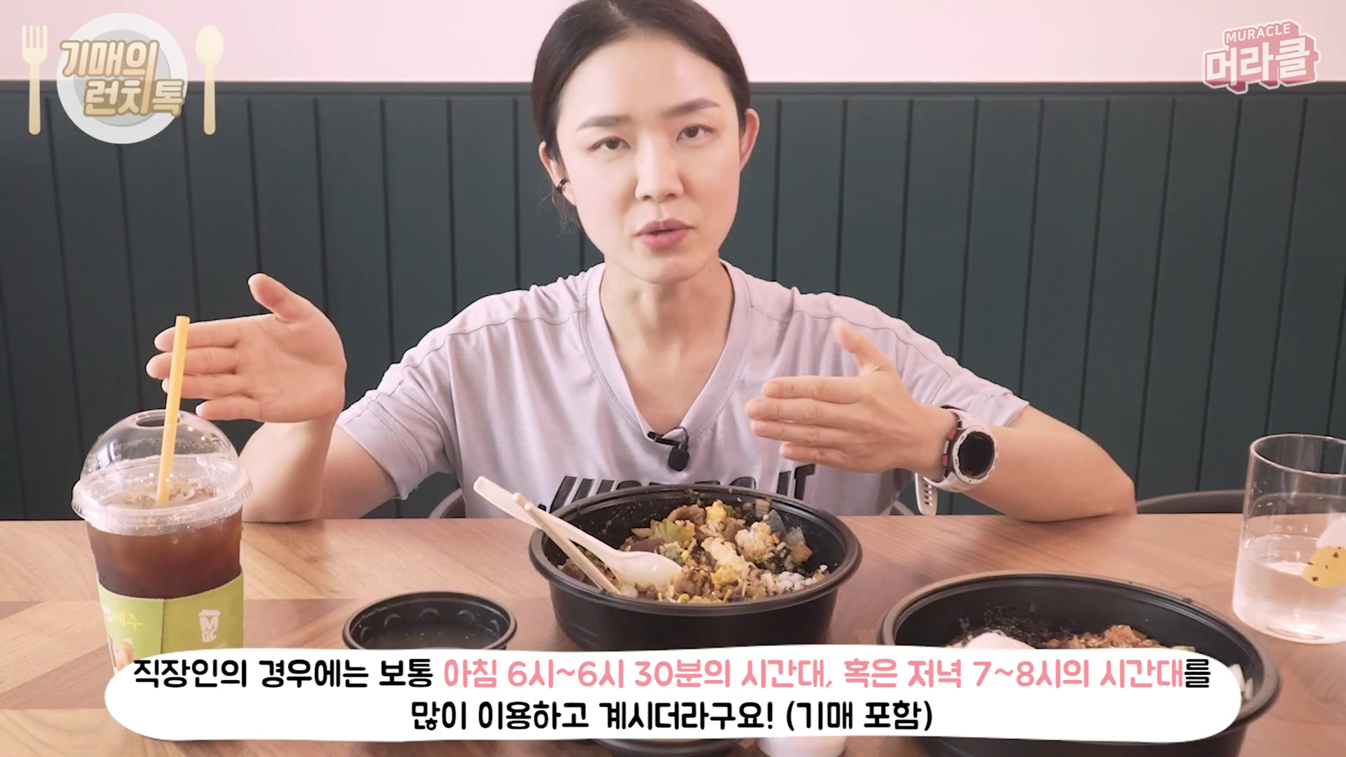 운동복 차림의 여성이 테이블에 앉아 손짓하며 대화를 나누고 있고, 앞에는 비빔밥 용기와 아이스 아메리카노가 놓여 있습니다.