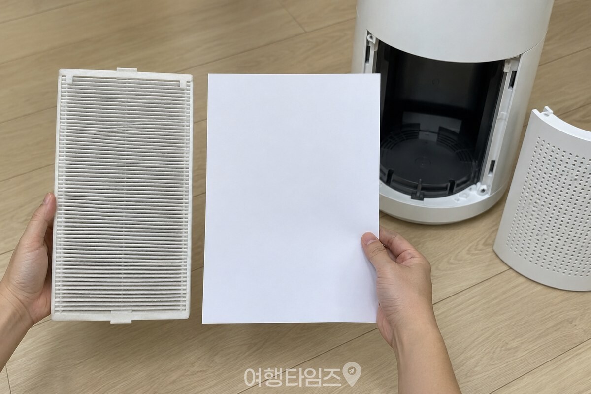 거실 바닥에 놓인 공기청정기에서 필터를 꺼내 A4 용지와 색을 비교하는 모습. / 기사 이해를 돕기 위한 생성형 이미지