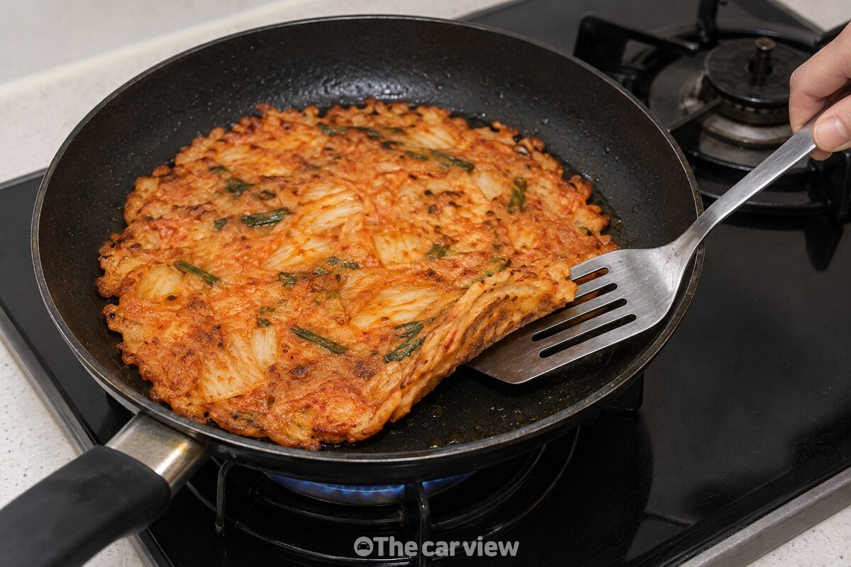 중약불에서 가장자리가 노릇해진 김치전의 아랫면을 뒤집개로 살짝 확인하는 모습. / 기사 이해를 돕기 위한 생성형 이미지