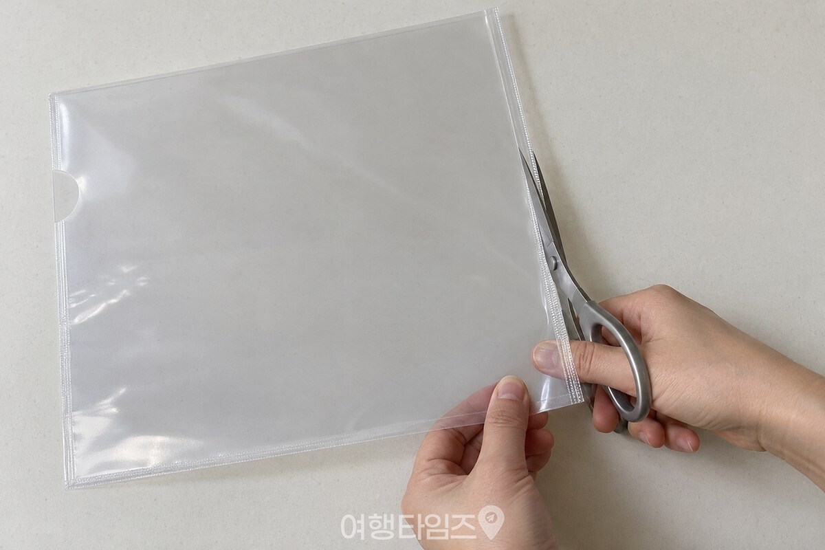 책상 위에 놓인 투명 L자 파일의 닫힌 긴 테두리를 가위로 곧게 자르고 있다. / 기사 이해를 돕기 위한 생성형 이미지