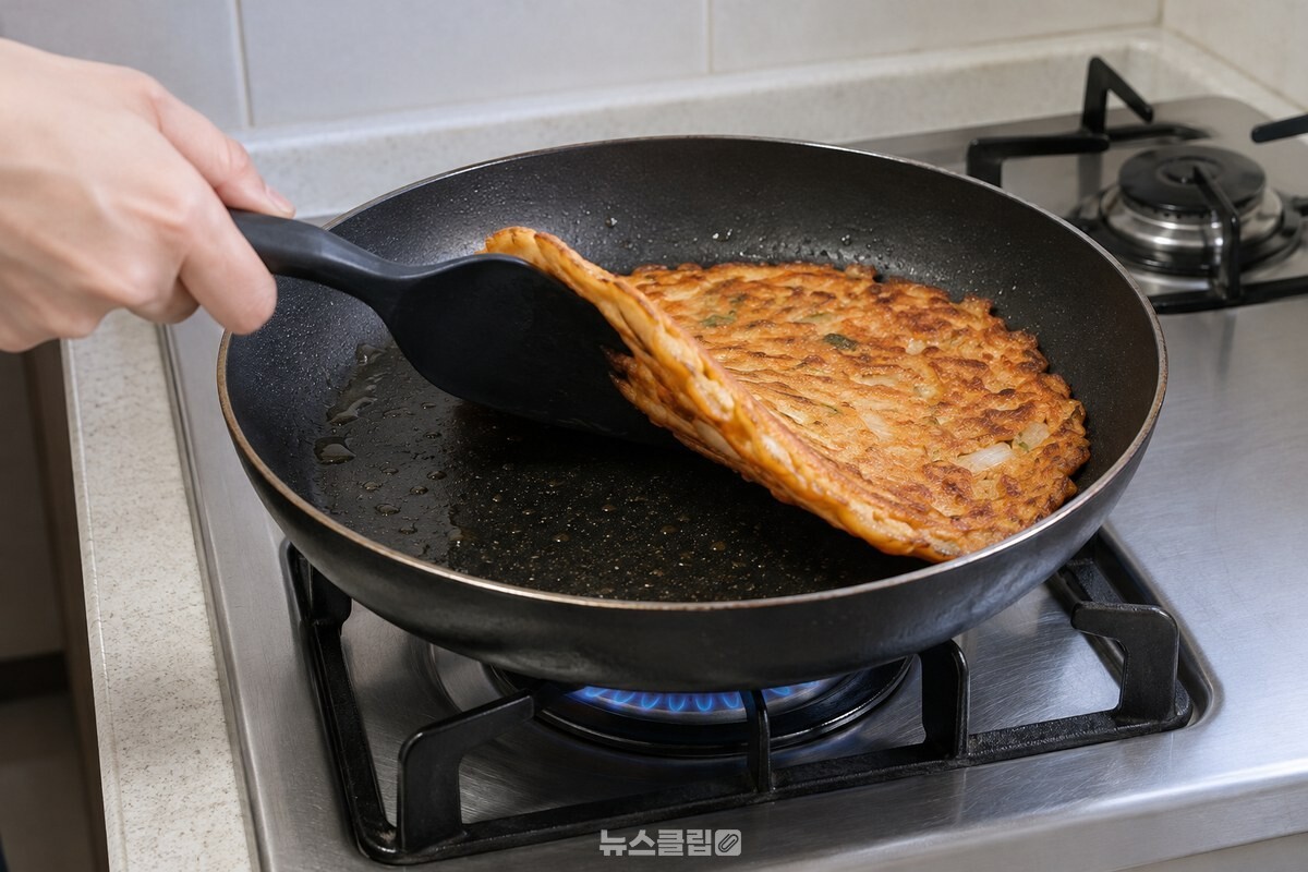 뒤집개로 김치전을 들어 빵가루를 뿌린 면이 팬 쪽으로 향하게 뒤집고 있다. / 기사 이해를 돕기 위한 생성형 이미지