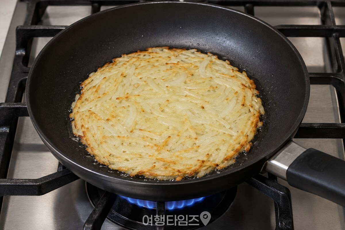 검은 프라이팬에서 얇게 펼친 감자전의 가장자리가 노릇하게 익고 있다. / 기사 이해를 돕기 위한 생성형 이미지