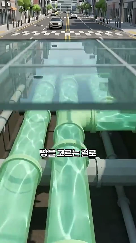 투명한 바닥 아래로 지하에 매설된 거대한 파이프라인과 물이 흐르는 모습이 보이고 그 위로 도로와 자동차들이 달리는 3D 그래픽 영상 화면.