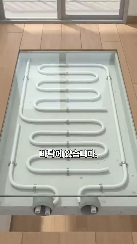 바닥재가 일부 걷어내지고 그 아래 매립된 흰색 보일러 난방 배관이 S자 형태로 배치된 모습.