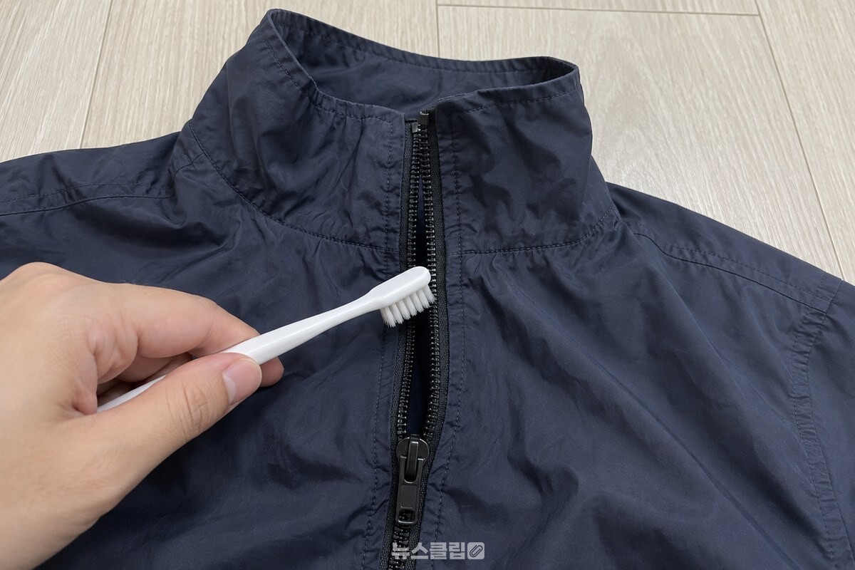 마른 칫솔로 바람막이 지퍼 이빨을 정리하는 손 / 기사 이해를 돕기 위한 생성형 이미지