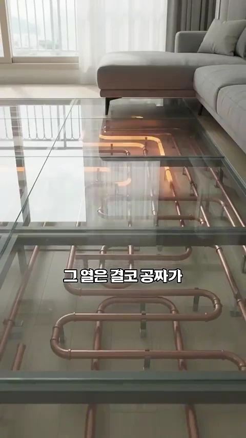 투명한 바닥 아래로 구리색 난방 배관들이 복잡하게 연결되어 있고, 그 위로 소파가 놓여 있는 거실 인테리어 CG 영상.