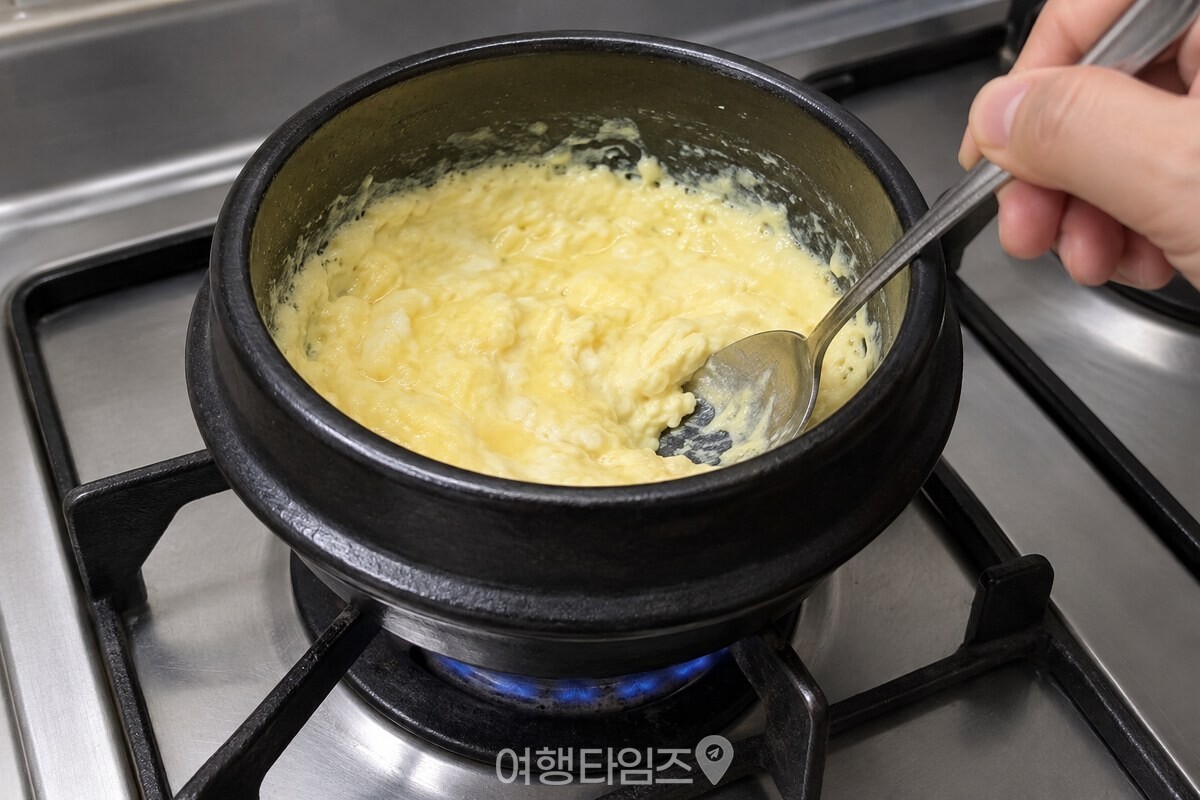 뚝배기 안에서 가장자리부터 부드럽게 익기 시작한 계란찜을 숟가락으로 저어 주는 장면 / 기사 이해를 돕기 위한 생성형 이미지