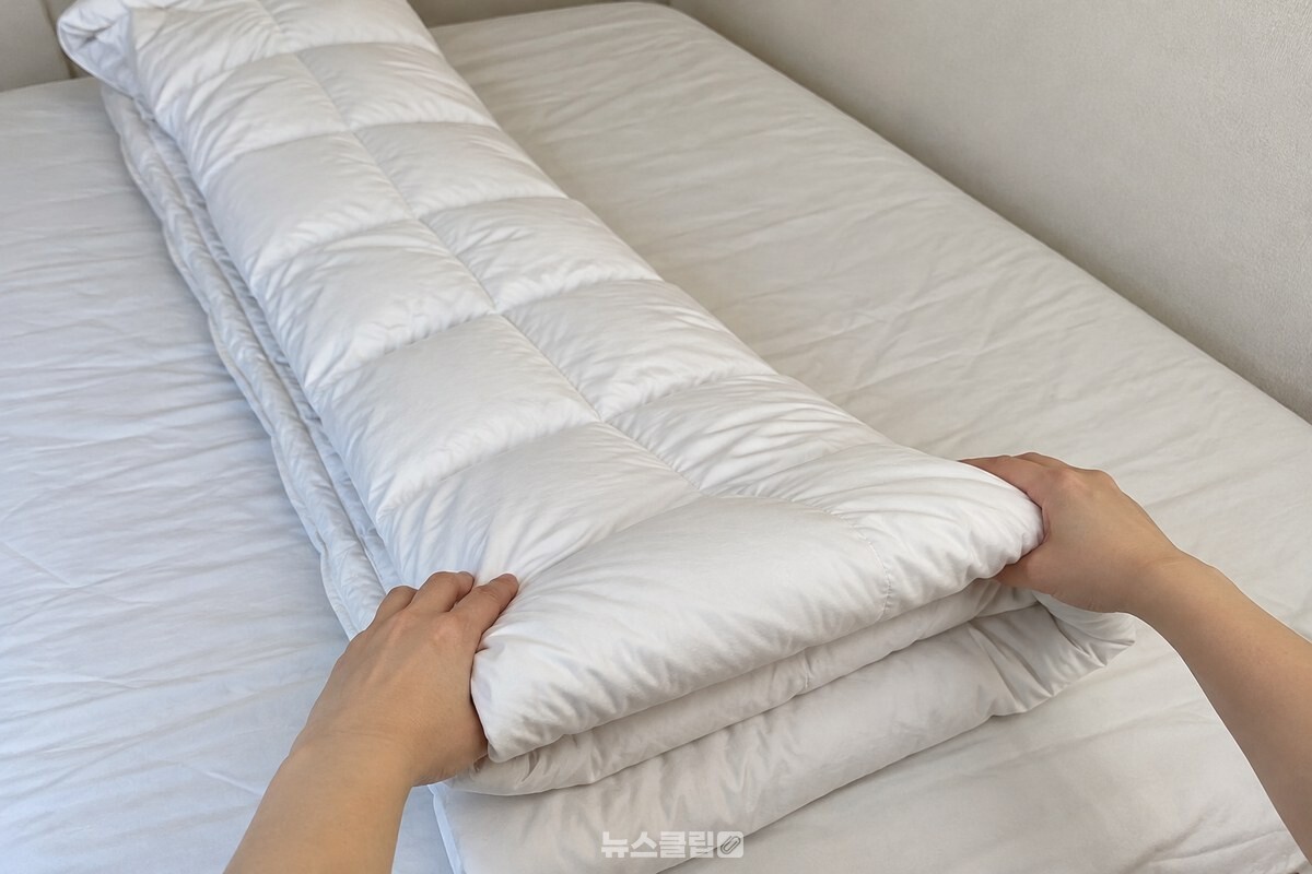 흰색 깃털 이불을 긴 띠 모양으로 접어 두툼한 사각형으로 만드는 과정. / 기사 이해를 돕기 위한 생성형 이미지