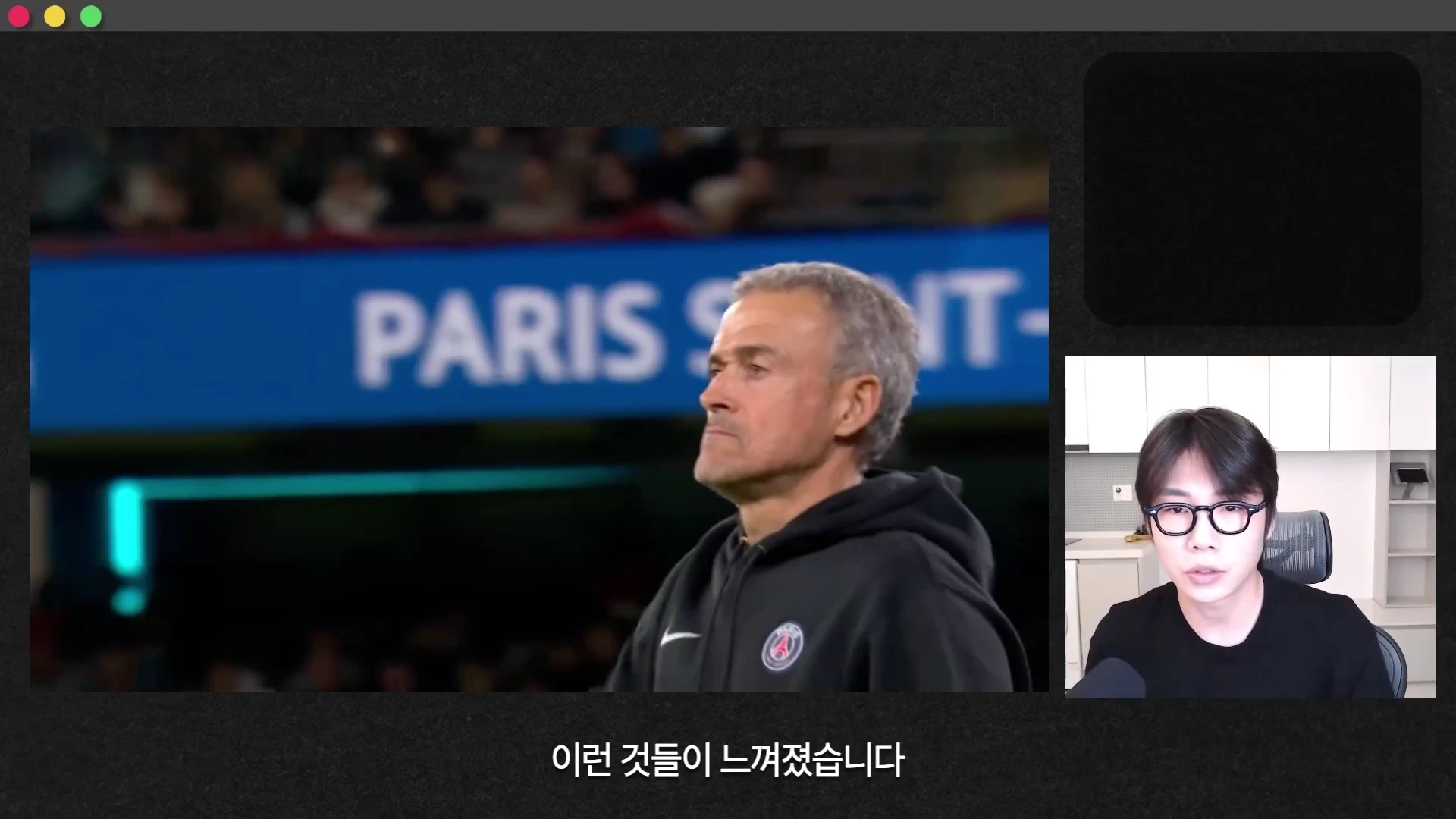 축구 경기장에서 파리 생제르맹 로고가 새겨진 검은색 후드티를 입고 서 있는 루이스 엔리케 감독의 모습과 화면 오른쪽에 안경을 쓴 남성 진행자가 말하는 모습이 담긴 영상 캡처 화면.