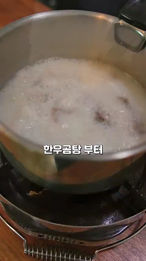 가스레인지 위 냄비에서 보글보글 끓고 있는 뽀얀 국물의 곰탕과 그 위에 적힌 '한우곰탕부터'라는 자막.