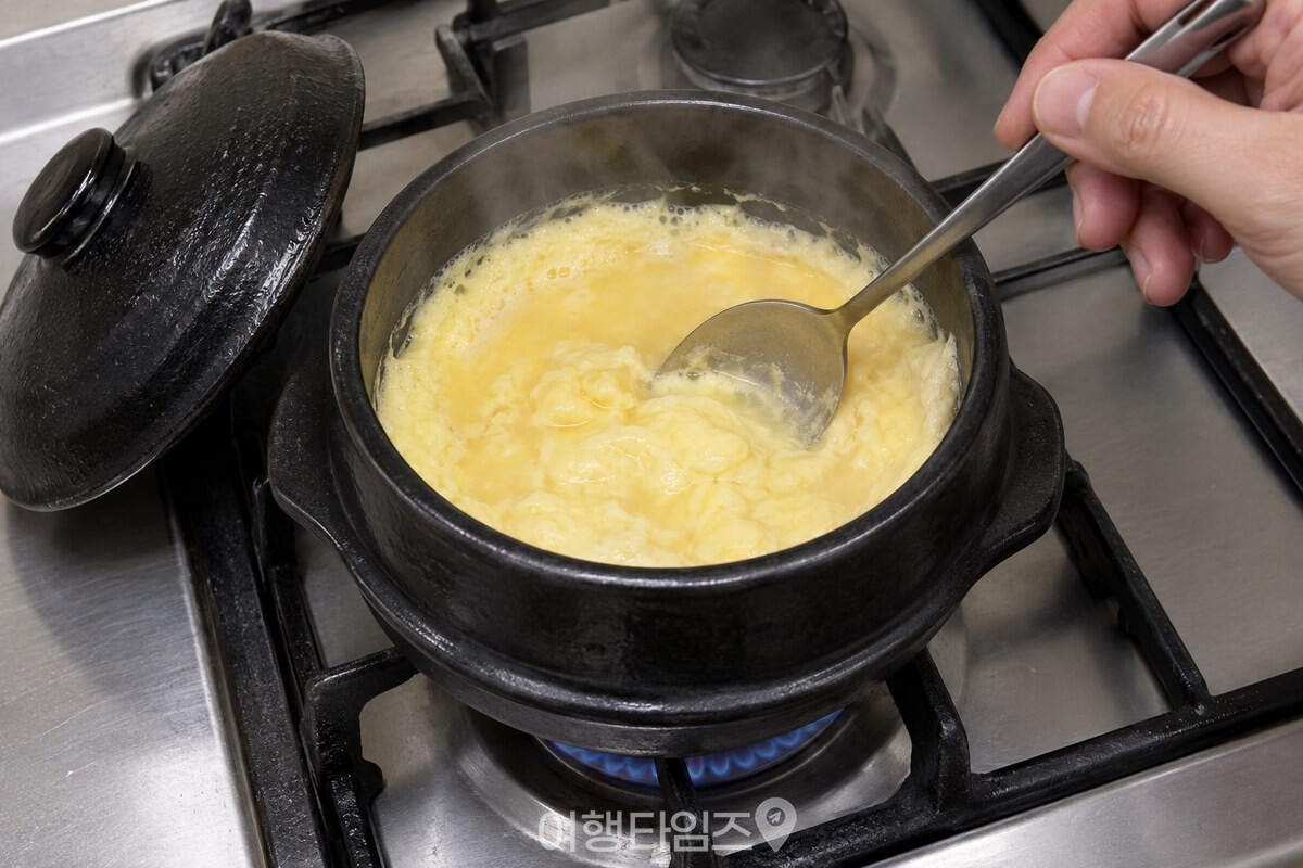 뚜껑을 연 뚝배기에서 익기 시작한 계란찜을 숟가락으로 한두 번 섞는 모습 / 기사 이해를 돕기 위한 생성형 이미지