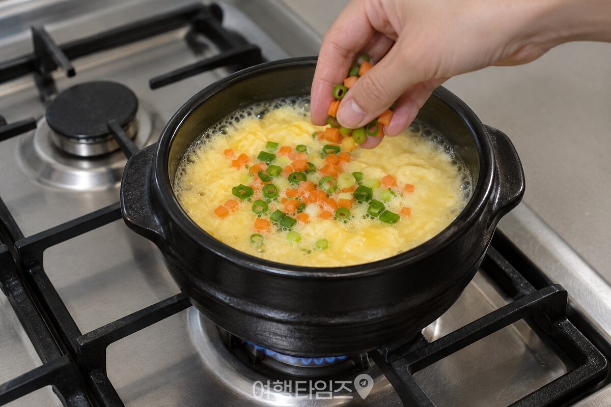 가장자리가 끓기 시작한 뚝배기 계란찜에 잘게 썬 채소를 올리는 모습. / 기사 이해를 돕기 위한 생성형 이미지